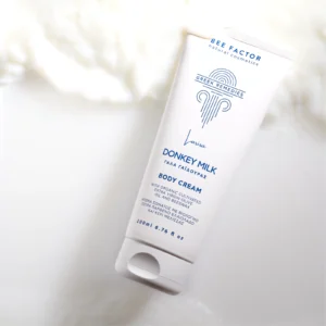 Witte tube Bee Factor-bodycrème met ezelinnenmelk op een witte, romige achtergrond.