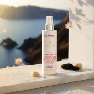 Een witte sprayflacon Essence of Santorini van Bee Factor bij een raam met uitzicht op zee en kiezels.