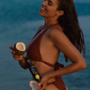 Vrouw aan zee met kokosnoten en Bee Factor Exotic Coconut-bruiningsolie.